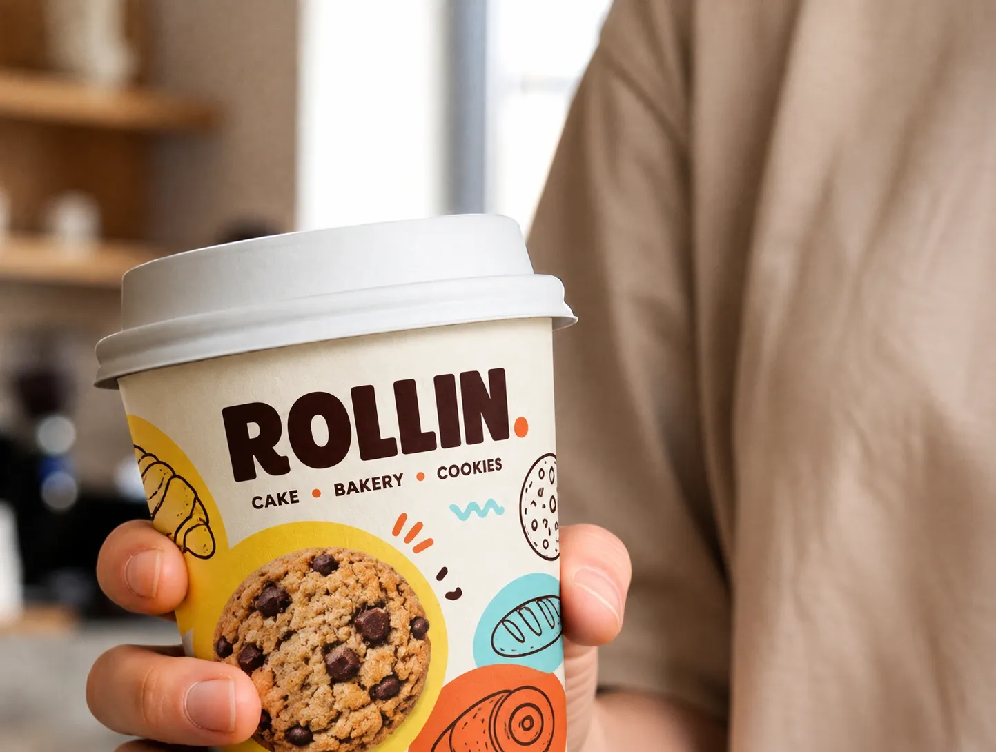Un gobelet Rollin décoré de cookies et de dessins, tenu à la main
